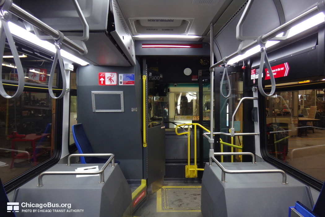 The interior of bus #7900 at CTA's South Shops Maintenance Facility on February  6, 2014. At the front of the bus, the most notable change from past CTA bus models is the more substantial protective barrier for bus operators. Elsewhere, the twin front seats behind the driver on CTA's previous generation Nova LFS buses have been replaced with a single, aisle-facing seat. Various computer equipment is located in a compartment suspended above this seat, necessitating a sign warning of the limited 175cm vertical clearance. Note the visible wiring for CTA's Ventra card reader, which was not yet installed at the time of this photograph.